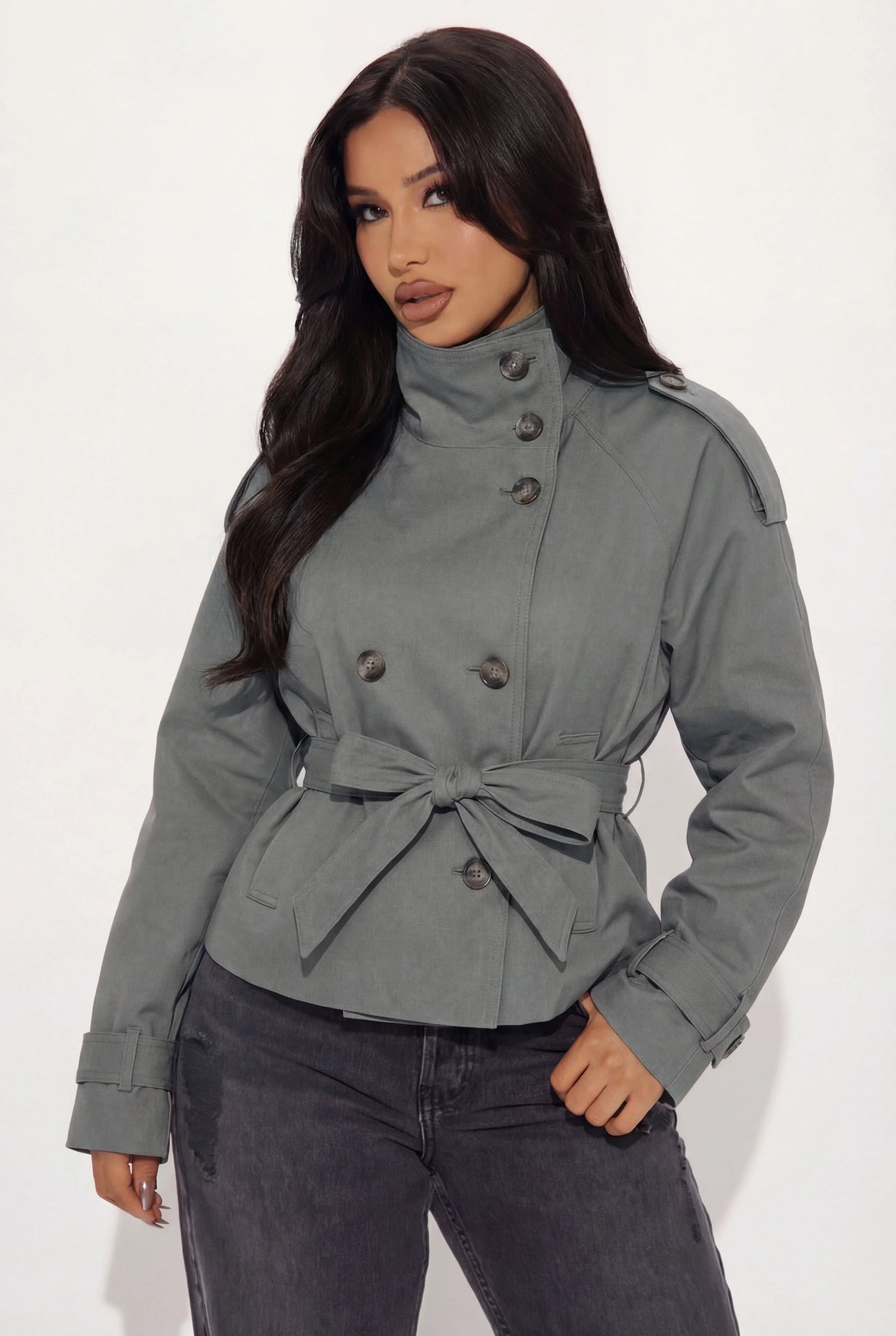 Grey - A woman wearing a beige cropped twill trench jacket with a high funnel neck, double-breasted button closure, and a cinched self-tie waist belt, paired with dark grey jeans.