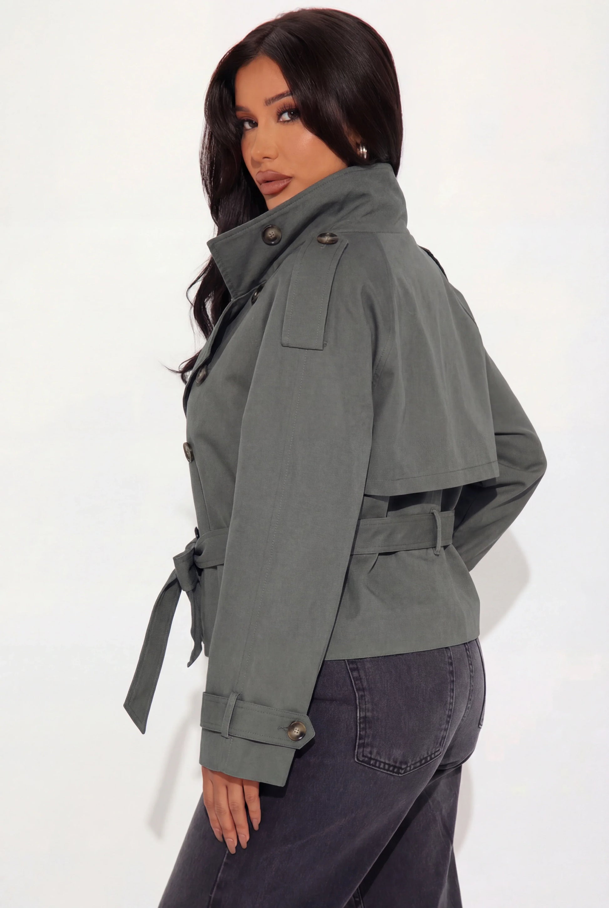 Grey - A woman wearing a beige cropped twill trench jacket with a high funnel neck, double-breasted button closure, and a cinched self-tie waist belt, paired with dark grey jeans.