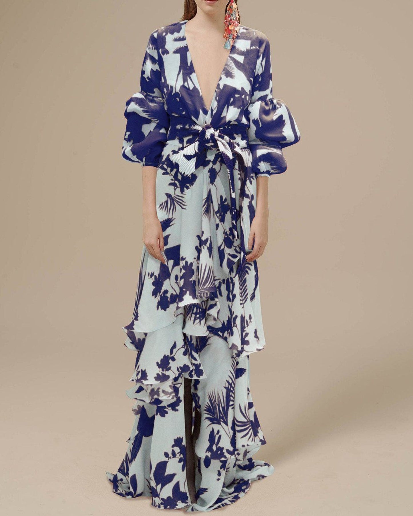 Blue - A woman wearing a pale blue and mustard yellow botanical print maxi dress featuring a deep V-neckline, voluminous balloon sleeves, a belted waist, and a cascading tiered ruffle skirt.