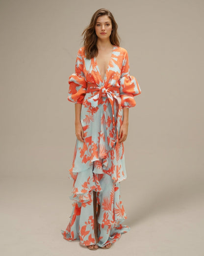 Orange - A woman wearing a pale blue and mustard yellow botanical print maxi dress featuring a deep V-neckline, voluminous balloon sleeves, a belted waist, and a cascading tiered ruffle skirt.