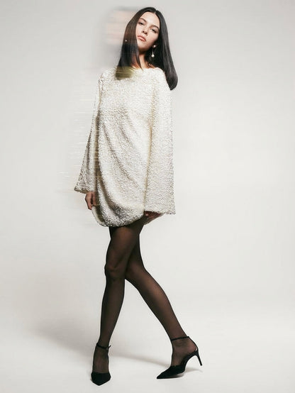 White - Model wearing a cream-coloured, highly textured bouclé knit mini dress with a high neckline, long sleeves, and an A-line silhouette, paired with black pointed-toe heels.