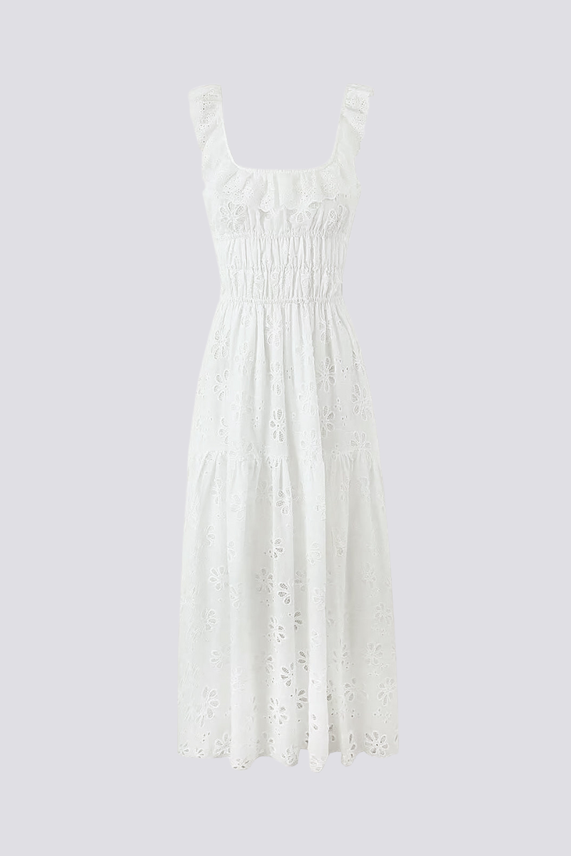White - A woman wearing a white broderie anglaise maxi dress with a ruffled neckline, smocked waist, and a high thigh slit.