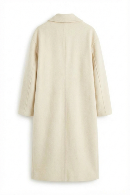 Beige - A woman wearing a camel-coloured, double-breasted longline coat with notch lapels and folded cuffs, styled over a striped sweater, blue jeans, and black boots against a white background.
