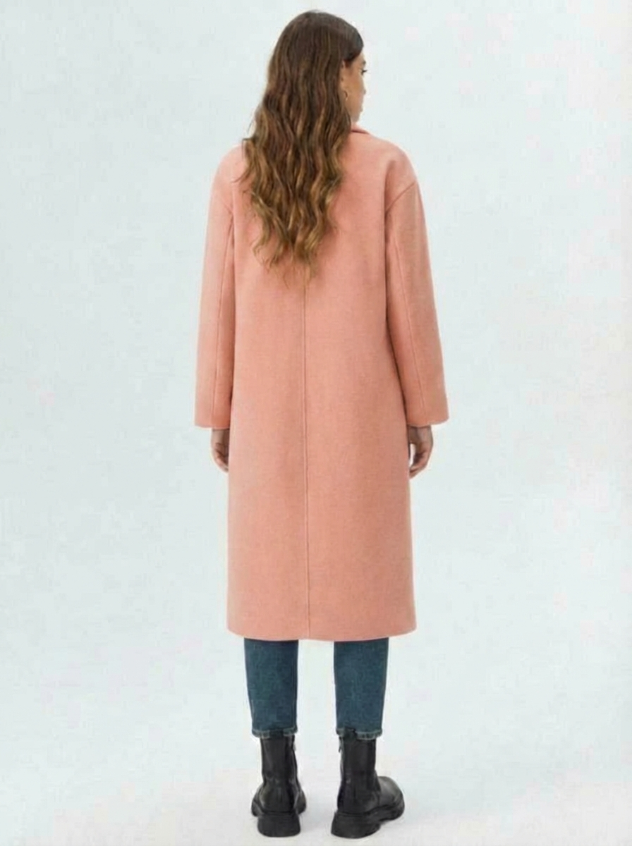 Pink - A woman wearing a camel-coloured, double-breasted longline coat with notch lapels and folded cuffs, styled over a striped sweater, blue jeans, and black boots against a white background.