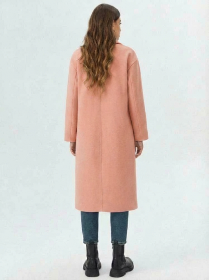 Pink - A woman wearing a camel-coloured, double-breasted longline coat with notch lapels and folded cuffs, styled over a striped sweater, blue jeans, and black boots against a white background.