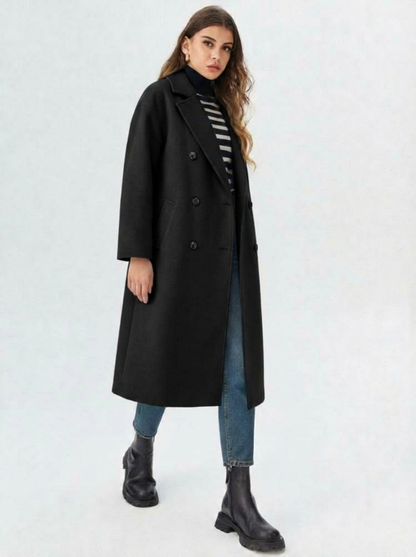Black - A woman wearing a camel-coloured, double-breasted longline coat with notch lapels and folded cuffs, styled over a striped sweater, blue jeans, and black boots against a white background.