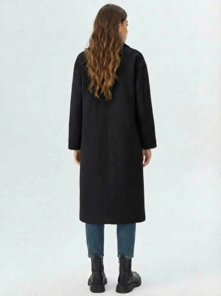Black - A woman wearing a camel-coloured, double-breasted longline coat with notch lapels and folded cuffs, styled over a striped sweater, blue jeans, and black boots against a white background.