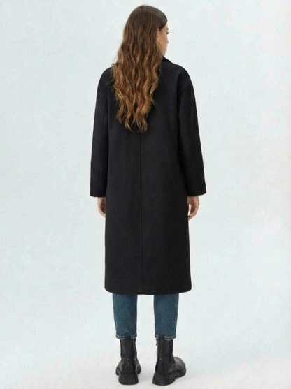 Black - A woman wearing a camel-coloured, double-breasted longline coat with notch lapels and folded cuffs, styled over a striped sweater, blue jeans, and black boots against a white background.