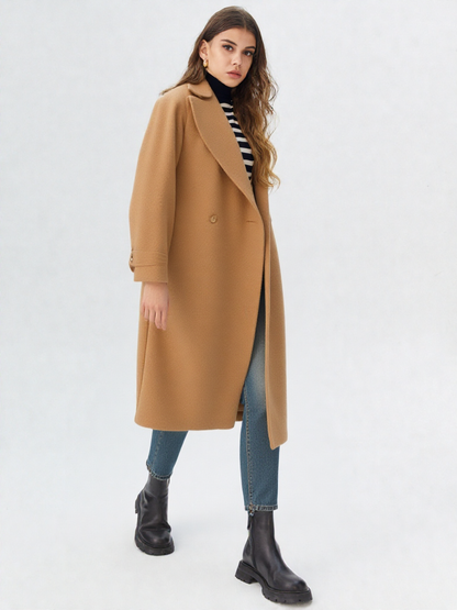 Brown - A woman wearing a camel-coloured, double-breasted longline coat with notch lapels and folded cuffs, styled over a striped sweater, blue jeans, and black boots against a white background.