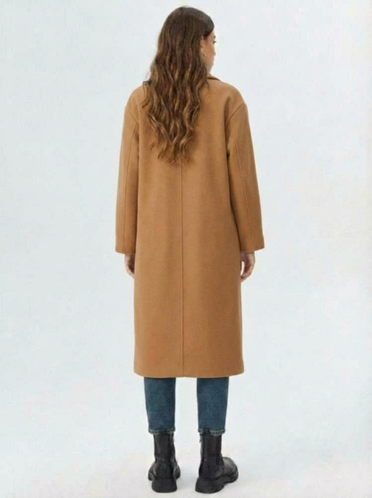 Brown - A woman wearing a camel-coloured, double-breasted longline coat with notch lapels and folded cuffs, styled over a striped sweater, blue jeans, and black boots against a white background.