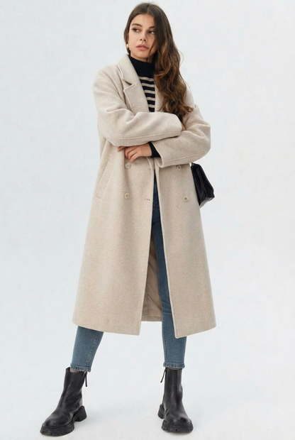 Brown - A woman wearing a camel-coloured, double-breasted longline coat with notch lapels and folded cuffs, styled over a striped sweater, blue jeans, and black boots against a white background.
