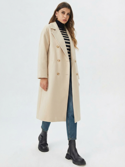 Beige - A woman wearing a camel-coloured, double-breasted longline coat with notch lapels and folded cuffs, styled over a striped sweater, blue jeans, and black boots against a white background.