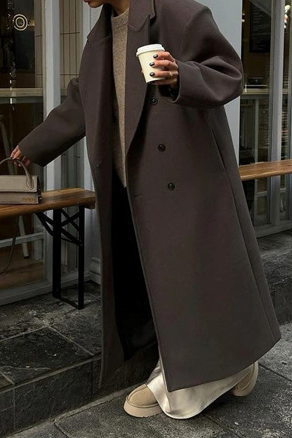 Brown - A person wearing a longline, double-breasted dark chocolate brown overcoat with notch lapels, styled over a beige knit sweater and cream silk skirt.