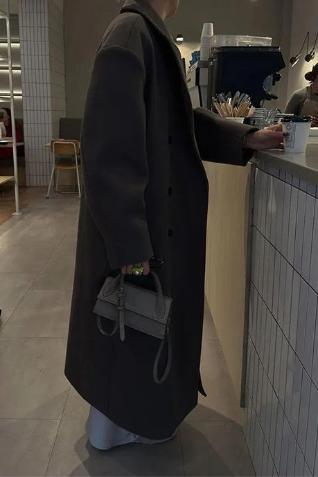 Brown - A person wearing a longline, double-breasted dark chocolate brown overcoat with notch lapels, styled over a beige knit sweater and cream silk skirt.