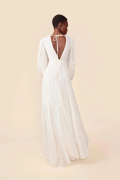 WHite - A woman stands outdoors near a pond wearing a long, flowing white maxi dress with a deep V-neck, ruched bodice, voluminous long sleeves, and an intricate burnout texture pattern.