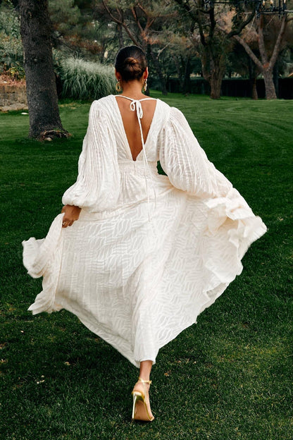 WHite - A woman stands outdoors near a pond wearing a long, flowing white maxi dress with a deep V-neck, ruched bodice, voluminous long sleeves, and an intricate burnout texture pattern.