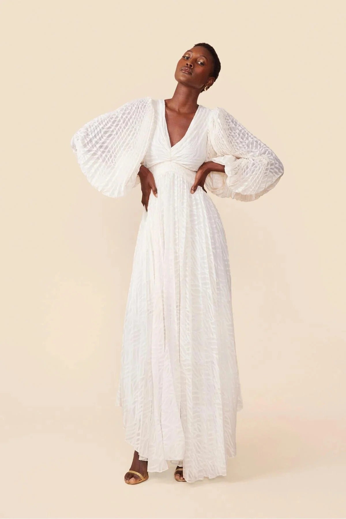 WHite - A woman stands outdoors near a pond wearing a long, flowing white maxi dress with a deep V-neck, ruched bodice, voluminous long sleeves, and an intricate burnout texture pattern.