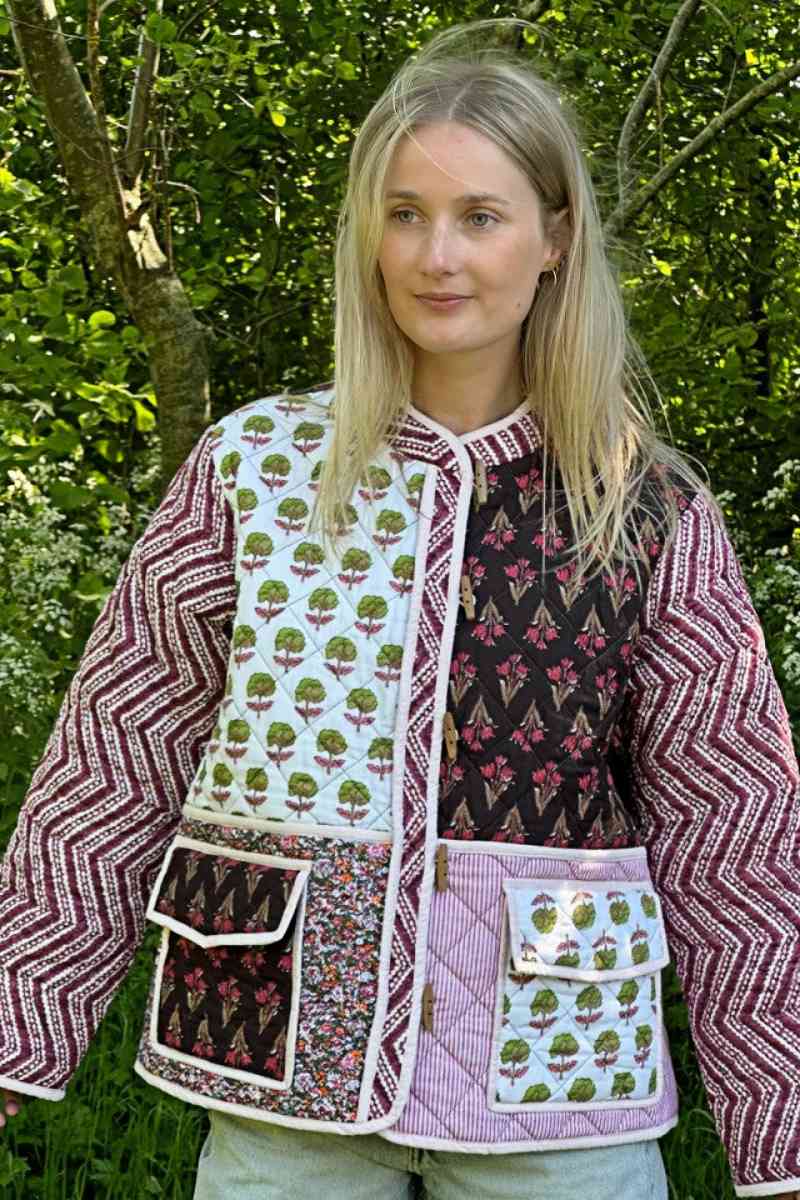 Woman wearing a quilted patchwork jacket featuring mixed floral and chevron prints, paired with a white maxi skirt.