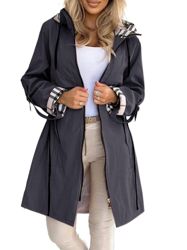 Blue - A woman wearing a taupe mid-length hooded jacket with a black zip front, featuring a distinctive black, white, and red check lining visible in the hood and rolled cuffs.
