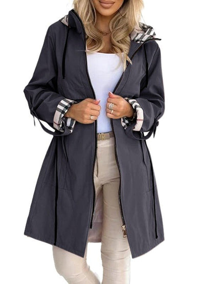 Blue - A woman wearing a taupe mid-length hooded jacket with a black zip front, featuring a distinctive black, white, and red check lining visible in the hood and rolled cuffs.