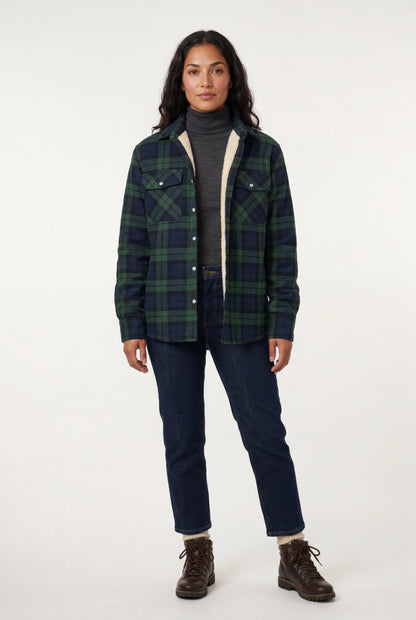 Green - A woman wearing a brown plaid flannel shirt jacket with a cream shearling lining, paired with dark wash jeans and brown leather boots.