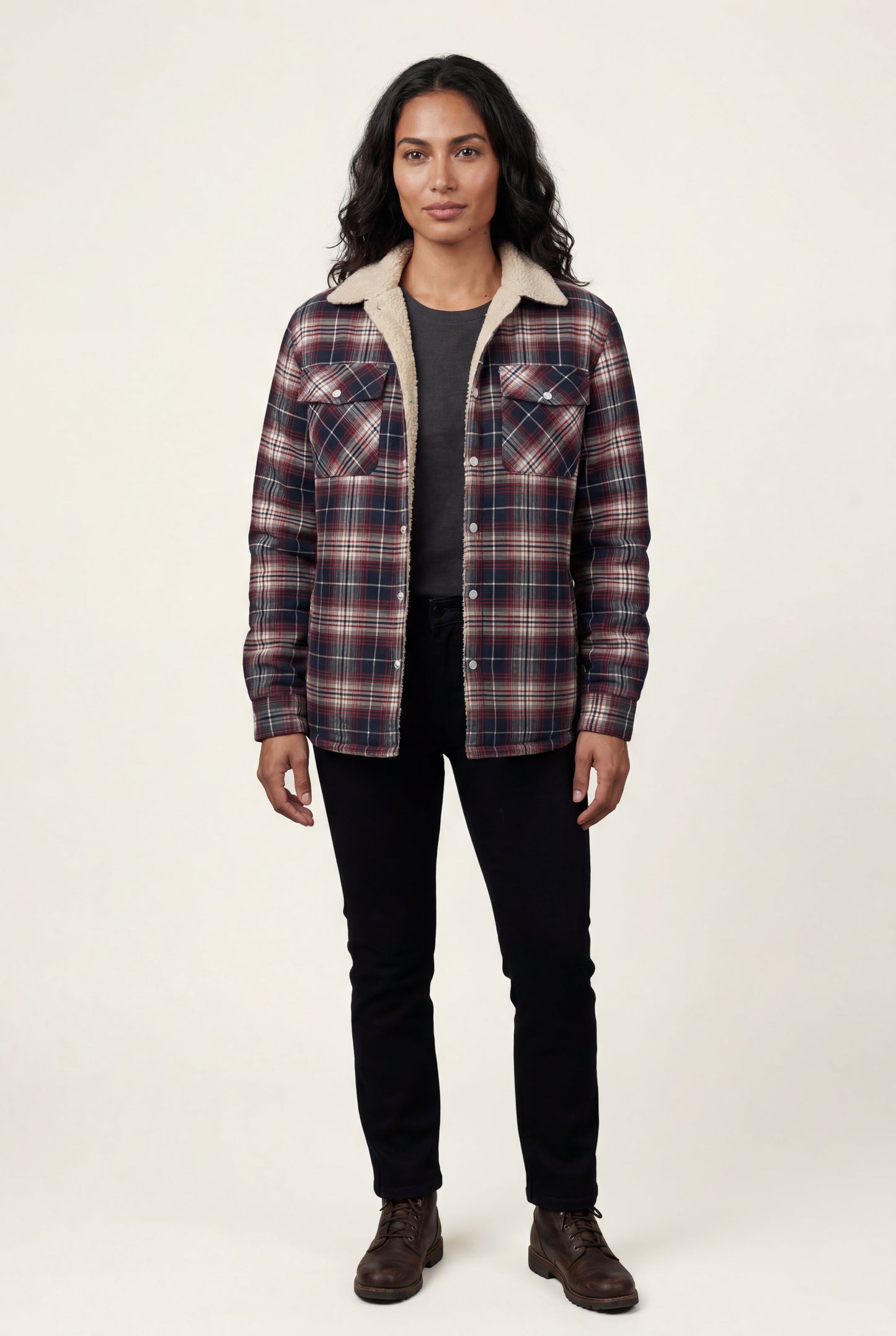 Denim Blue - A woman wearing a brown plaid flannel shirt jacket with a cream shearling lining, paired with dark wash jeans and brown leather boots.