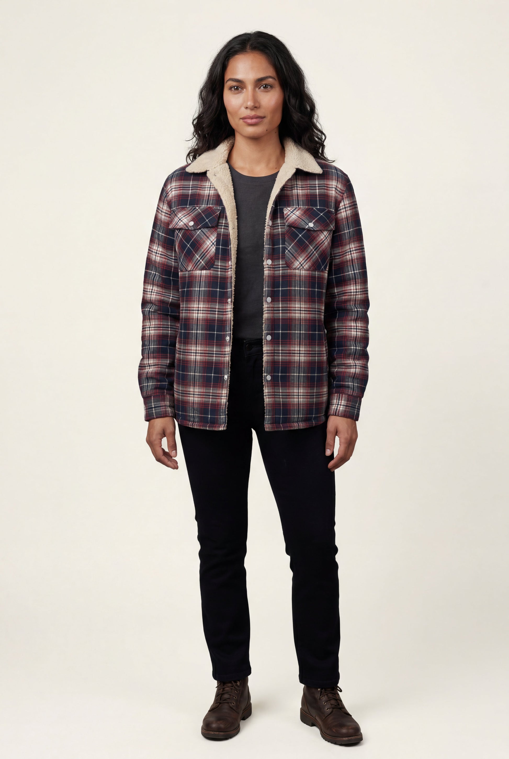 Denim Blue - A woman wearing a brown plaid flannel shirt jacket with a cream shearling lining, paired with dark wash jeans and brown leather boots.
