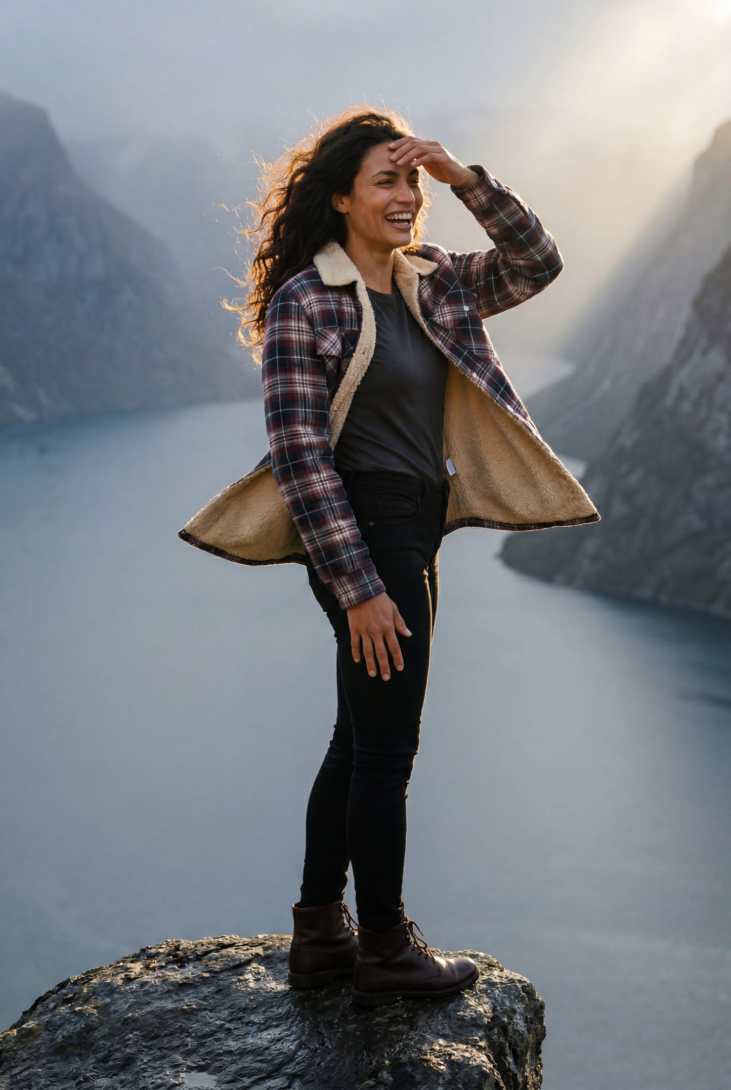 Denim Blue - A woman wearing a brown plaid flannel shirt jacket with a cream shearling lining, paired with dark wash jeans and brown leather boots.