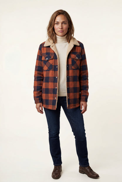 Orange - A woman wearing a brown plaid flannel shirt jacket with a cream shearling lining, paired with dark wash jeans and brown leather boots.