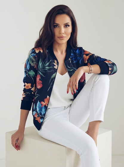 Blue - A woman wearing a white bomber jacket featuring a detailed pink cherry blossom and green leaf print, styled with black pants against a neutral grey background.