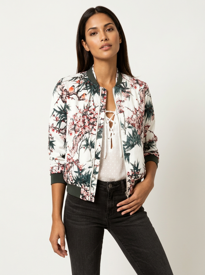 White - A woman wearing a white bomber jacket featuring a detailed pink cherry blossom and green leaf print, styled with black pants against a neutral grey background.