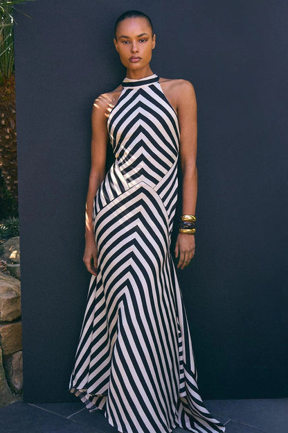 A woman wearing a black and white chevron-striped halter neck maxi dress against a dark grey background.