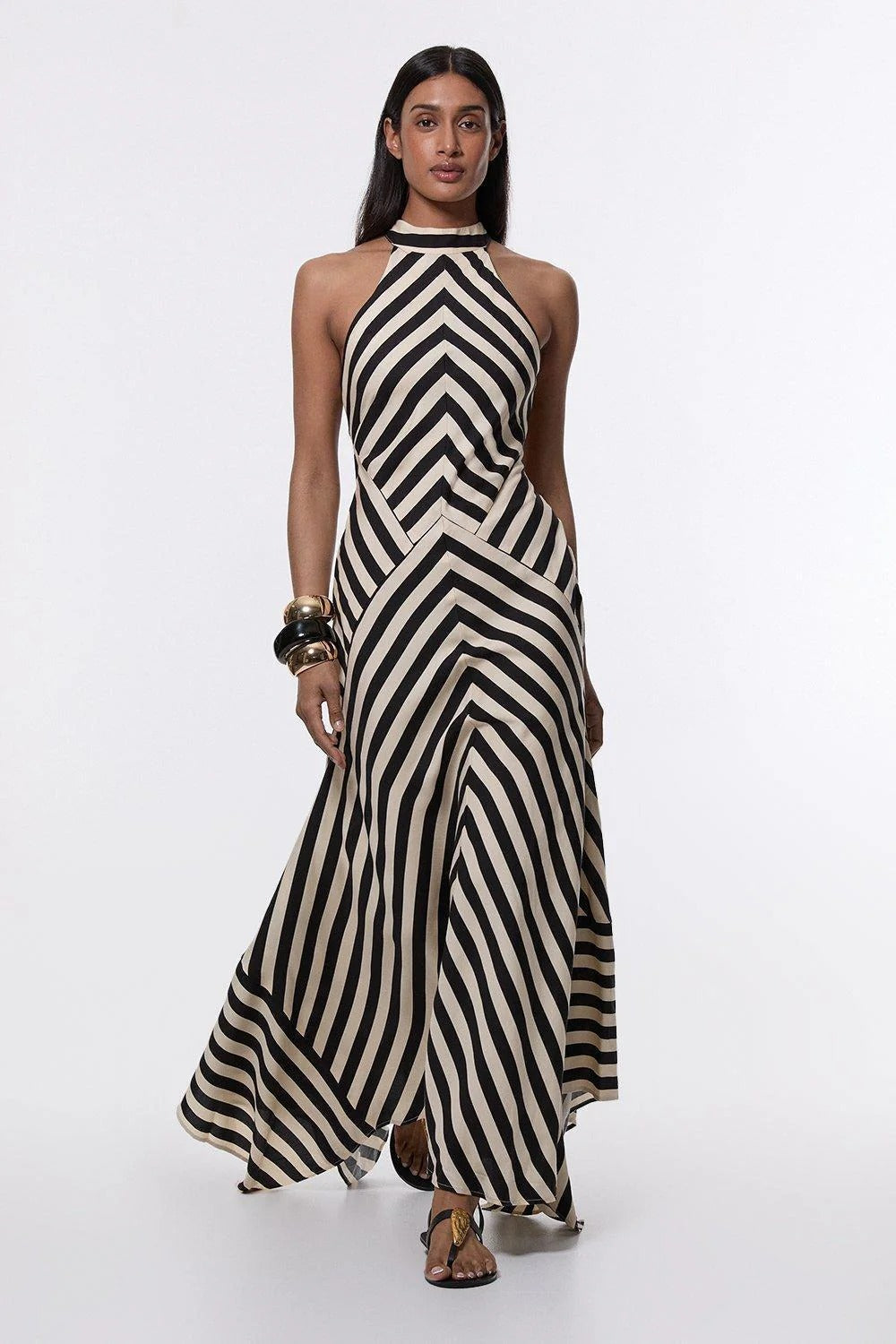 A woman wearing a black and white chevron-striped halter neck maxi dress against a dark grey background.