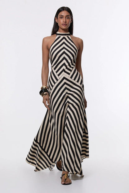 A woman wearing a black and white chevron-striped halter neck maxi dress against a dark grey background.