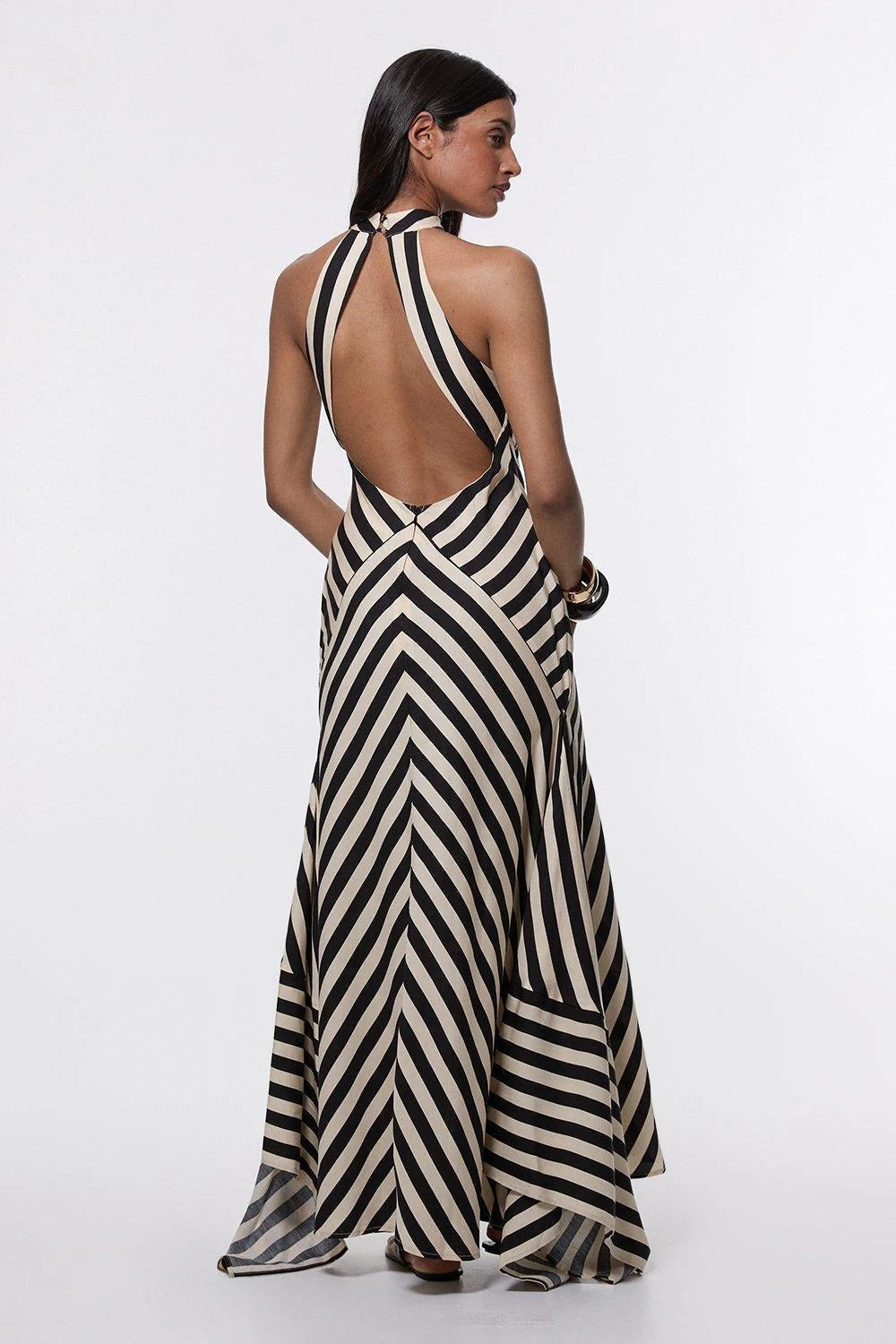 A woman wearing a black and white chevron-striped halter neck maxi dress against a dark grey background.
