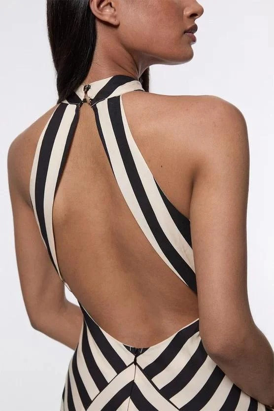 A woman wearing a black and white chevron-striped halter neck maxi dress against a dark grey background.