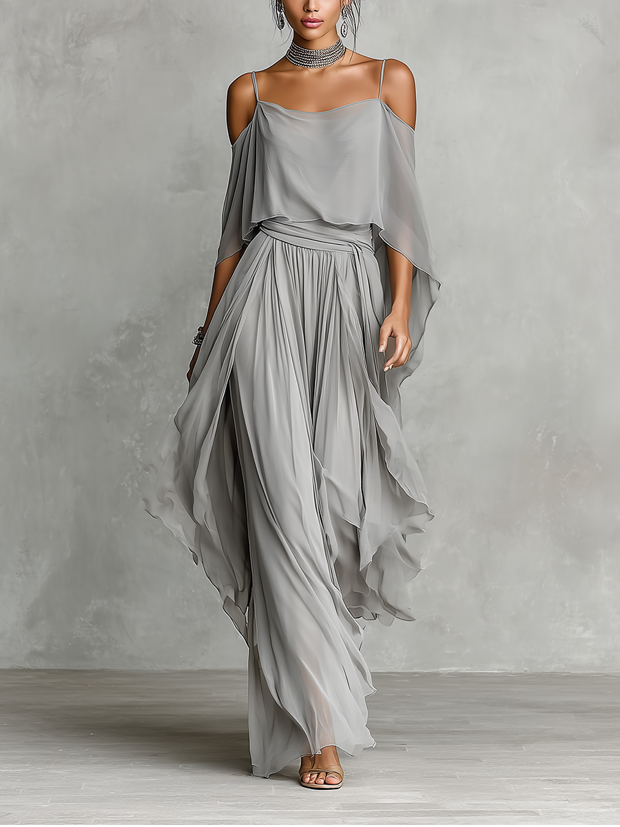 Grey - A model wears a floor-length grey chiffon maxi dress featuring delicate spaghetti straps, a draped cold-shoulder overlay, a ruched waist, and a layered, flowing skirt.
