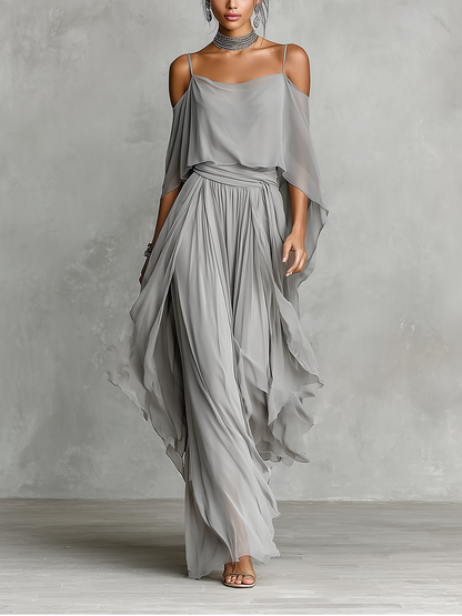 Grey - A model wears a floor-length grey chiffon maxi dress featuring delicate spaghetti straps, a draped cold-shoulder overlay, a ruched waist, and a layered, flowing skirt.