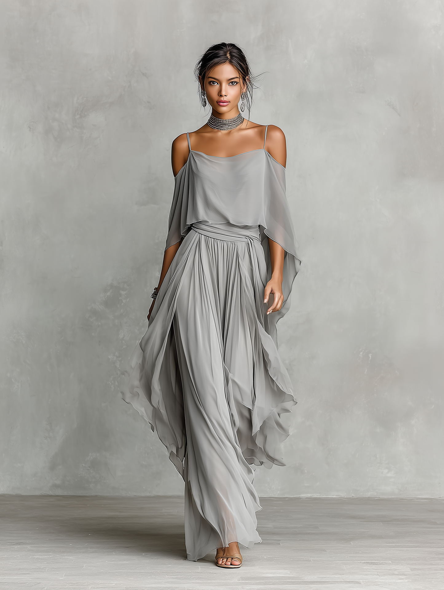 Grey - A model wears a floor-length grey chiffon maxi dress featuring delicate spaghetti straps, a draped cold-shoulder overlay, a ruched waist, and a layered, flowing skirt.