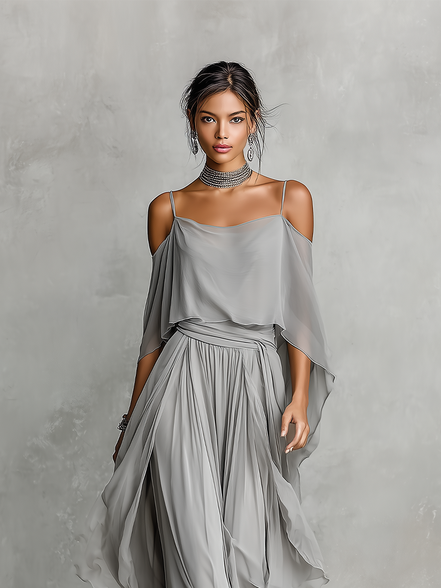 Grey - A model wears a floor-length grey chiffon maxi dress featuring delicate spaghetti straps, a draped cold-shoulder overlay, a ruched waist, and a layered, flowing skirt.