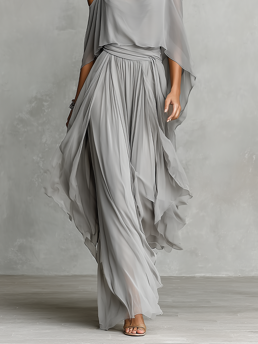 Grey - A model wears a floor-length grey chiffon maxi dress featuring delicate spaghetti straps, a draped cold-shoulder overlay, a ruched waist, and a layered, flowing skirt.