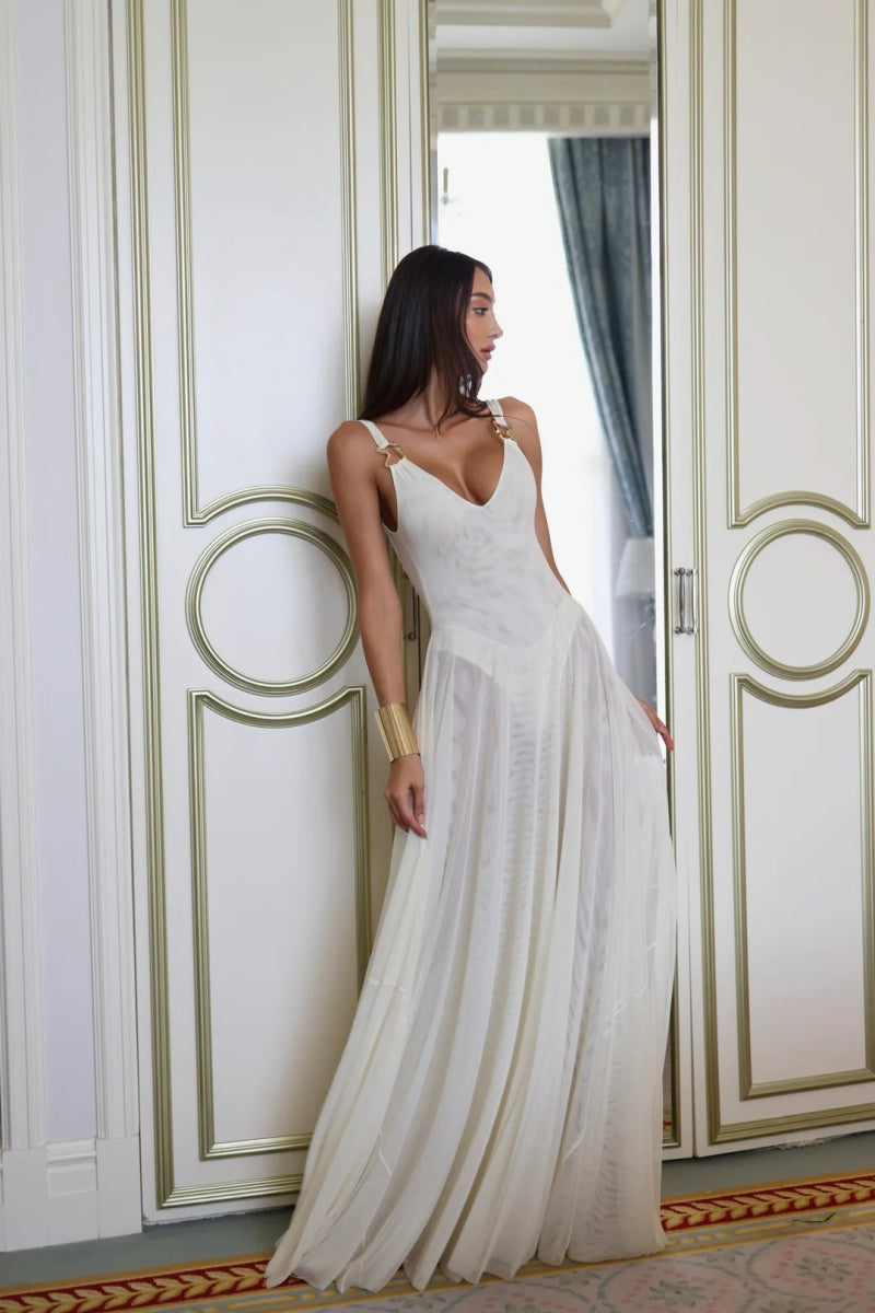 White - A woman wearing an elegant off-white maxi dress featuring a structured plunging bodice with gold hardware shoulder straps and a sheer, flowing pleated chiffon skirt.