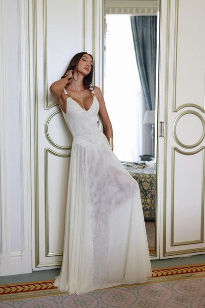 White - A woman wearing an elegant off-white maxi dress featuring a structured plunging bodice with gold hardware shoulder straps and a sheer, flowing pleated chiffon skirt.