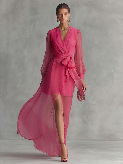 Pink - A woman wearing a rose pink long-sleeve chiffon maxi dress with a plunging V-neckline, a tied waist belt, and a high leg split, walking forward as the lightweight fabric drapes and flows.