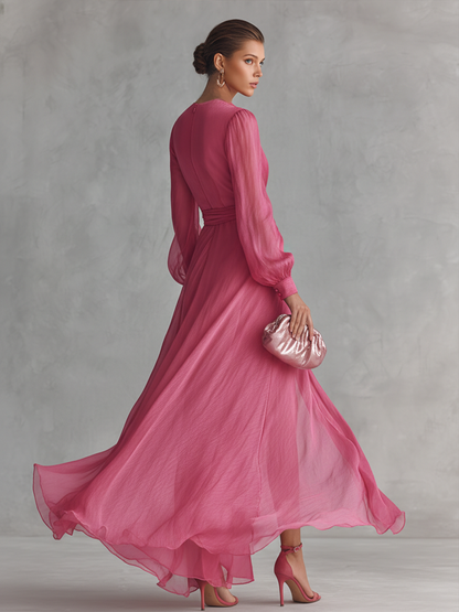 Pink - A woman wearing a rose pink long-sleeve chiffon maxi dress with a plunging V-neckline, a tied waist belt, and a high leg split, walking forward as the lightweight fabric drapes and flows.