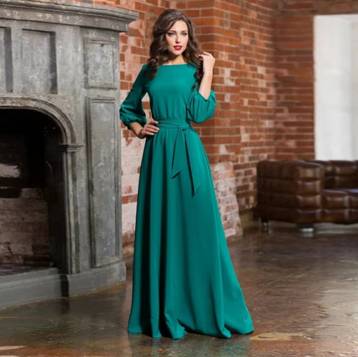 Dark Green - A woman posing in a floor-length white crepe maxi dress featuring a boat neckline, three-quarter balloon sleeves, and a self-tie fabric sash at the waist, set against a modern interior backdrop.