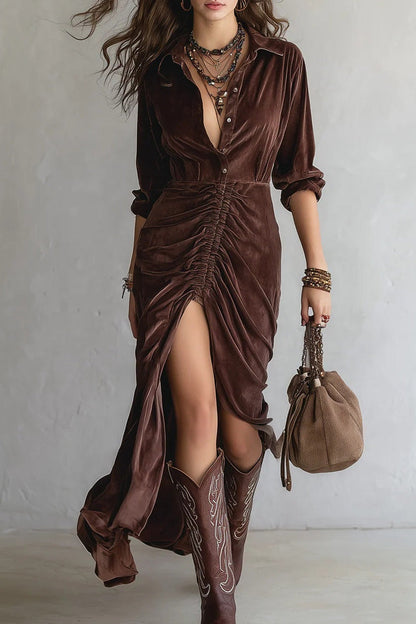 Brown - Woman walking wearing a long velvet dress with a collared neckline, button front, center ruching, and a high front slit, styled with tall western boots.