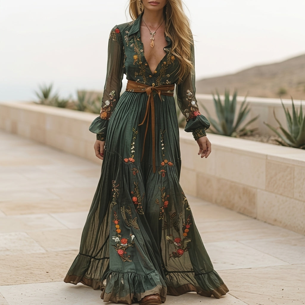 A woman wearing a dark green embroidered chiffon maxi dress with long balloon sleeves, a collared deep V-neckline, and a tiered pleated skirt, accessorised with a brown tie belt.