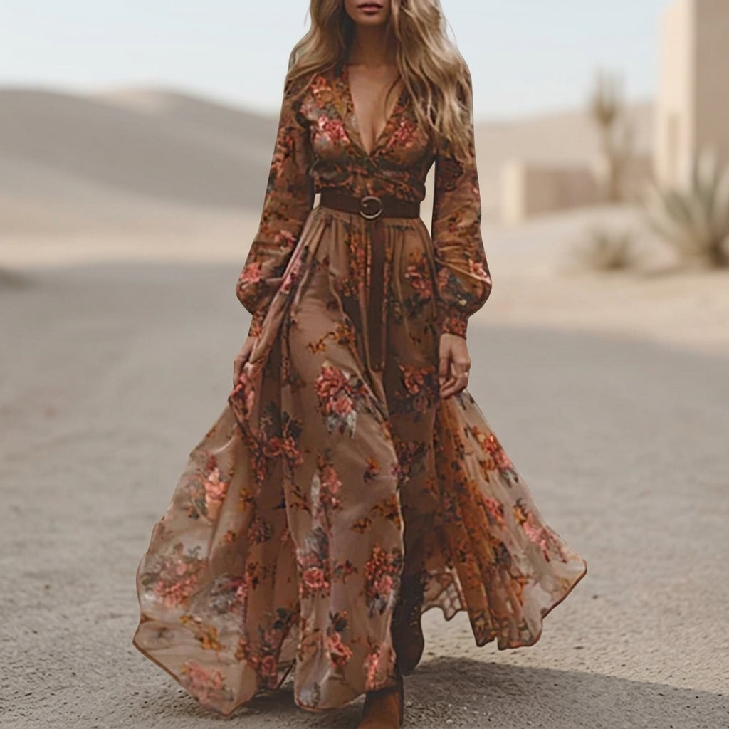 A woman wearing a dark green embroidered chiffon maxi dress with long balloon sleeves, a collared deep V-neckline, and a tiered pleated skirt, accessorised with a brown tie belt.