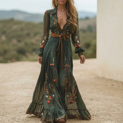 Green - A woman wearing a dark green embroidered chiffon maxi dress with long balloon sleeves, a collared deep V-neckline, and a tiered pleated skirt, accessorised with a brown tie belt.